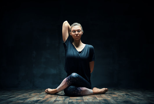 Young woman practicing yoga doing Gomukhasana ( cow face pose) in dark room. Wellbeing, meditation and healthy lifestyle