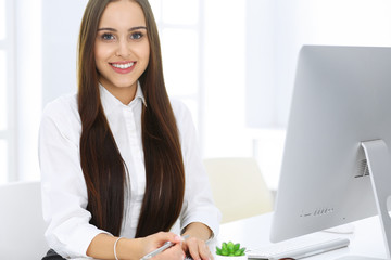 Business woman sitting and working with computer in white office. Student girl studying or secretary making report. Success concept