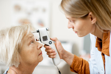 Female ophthalmologist measuring the eye pressure with modern tonometer to a senior patient in the medical office