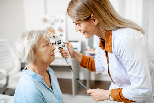 Female ophthalmologist measuring the eye pressure with modern tonometer to a senior patient in the medical office