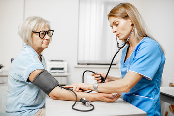 Nurse measuring blood pressure of a senior woman patient with tonometr during an examination in the clinic. Senior care concept