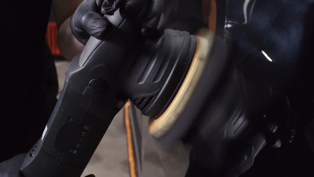 Handheld close up of hands of unrecognizable man in gloves using machine buffer and coating exterior of car with wax