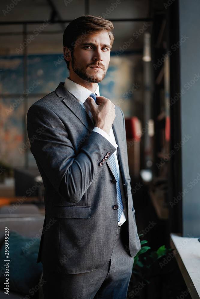 Canvas Prints stylish young bearded man in a suit is standing near the window and looking far