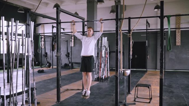 Handheld, wide pull-ups to chest. Middle-aged strong man pulls up on bar in gym, wears lift and grip gear. Fitness instructor is training. Strengthening muscles of back, body and chest