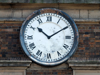 old round clock on the brick wall of a building with roman numerals with hands at ten past ten