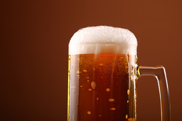 Close up pouring frothy beer in glass over brown