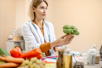 Nutritionist holding fresh broccoli, working on a diet plan in the office