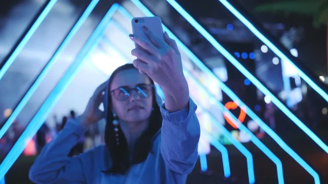 Woman on a neon party in the open air leads storis on smartphone.