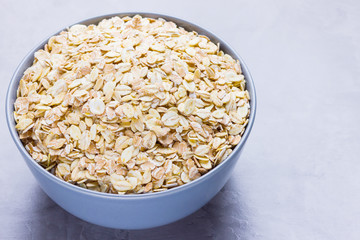 Dry oatmeal in bowl. Oat flakes on cement background. Cereals for making healthy breakfast