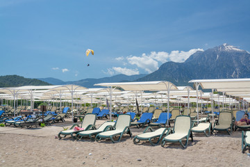 Sun loungers stand on a sandy beach on a background of snow-capped mountains.