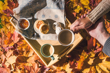 Couple of man and woman having morning breakfast in the autumn garden with colorful maple leaves. cup of coffee, marshmallow jam and a cheese pancake on a wooden tray.  Aerial view