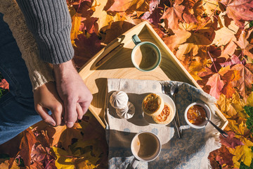 Couple of man and woman having morning breakfast in the autumn garden with colorful maple leaves. cup of coffee, marshmallow jam and a cheese pancake on a wooden tray.  Aerial view