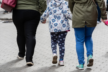 Two women and two children holding hands.  Only legs visible. Rear view