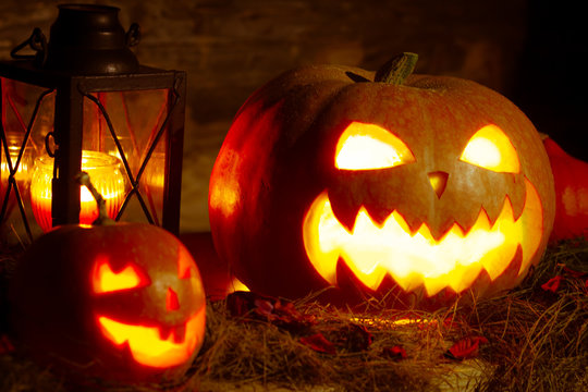 two halloween pumpkins with glowing eyes and creepy smiles in the dark, an old lantern with a candle, jack o lantern