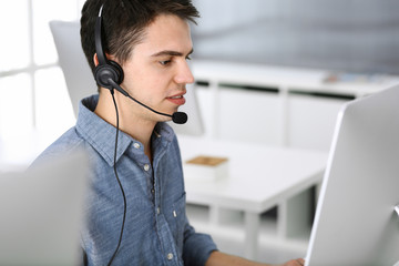 Group of operators at work. Call center. Focus on young man receptionist in headset at customer service. Business concept and casual clothing style