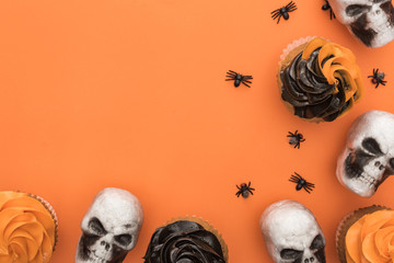 top view of Halloween cupcakes with spiders and skulls on orange background with copy space