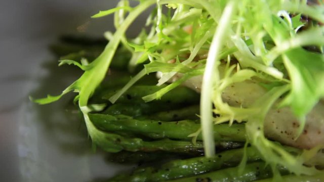 Close-up of blanched asparagus and grilled fillet of pike perch, served with lemon and herbs on a white plate.Macro