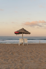 Sunrise on an empty beach with an sun umbrella and two chairs.