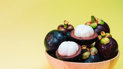 Mangosteen tropicl summer fruit in wood bowl isolated on yellow background.Queen of healthy fruit of Thailand.