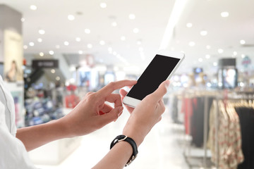 Woman hands holding and using smartphone with blank screen for your text or advertising isolated on blurred shopping mall interior background.Mock up phone mobile concept.
