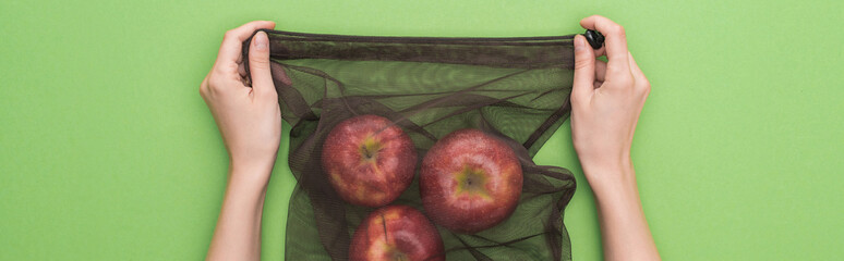 cropped view of woman holding apples in eco friendly bag isolated on green, panoramic shot