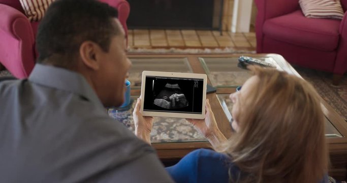 Over the shoulder shot of African American and Caucasian couple looking at ultrasound of grandchild. Senior husband and wife happy to be future grandparents. Slow motion 4k Handheld