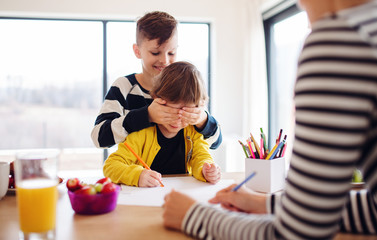 A young woman with two children drawing in a kitchen.