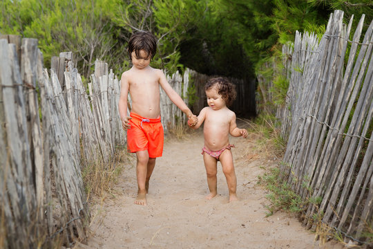 Young boy holding hands with toddler girl at beach