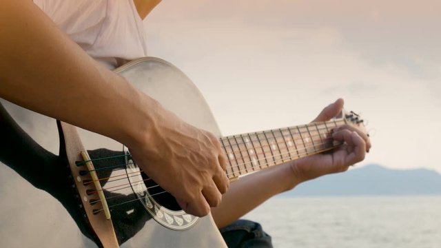 4K. close up of a man playing acoustic guitar at the beach during sunset time, feeling relax
