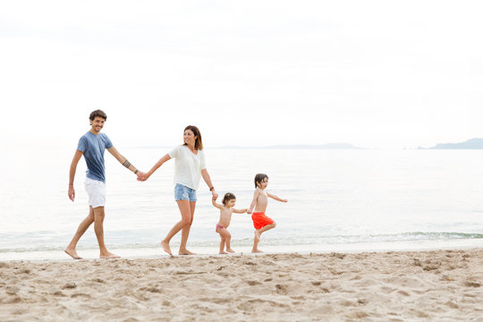 Playful family holding hands and walking in line at beach