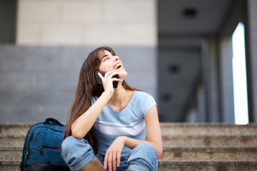 happy young woman sitting on steps talking with cellphone and bag