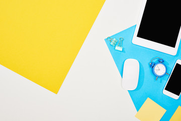 top view of smartphone, digital tablet with blank screen and computer mouse with office supplies on yellow, blue and white background