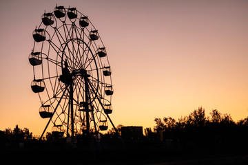 Silhouette of a ferris wheel at sunrise (sunset) of the sun on a background of trees and grass.