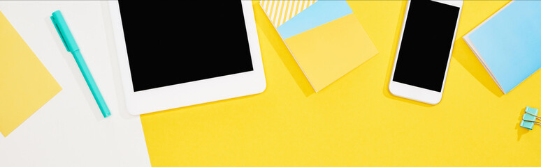 top view of digital tablet, smartphone with blank screen and office supplies on yellow and white background, panoramic shot