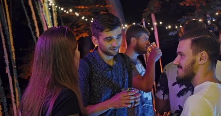 Circle of young stylish happy people socializing at summer holiday smiling enjoying celebration party at night.