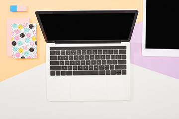 top view of laptop with blank screen, digital tablet and office supplies on beige, violet and white background