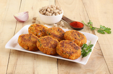 Kabuli chana tikkis, or chickpea patties, a healthy, vegetarian, delicious, and Indian food, with some of its ingredients, on a plate on a wooden background.