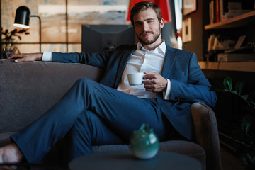 Handsome young man holding coffee cup sitting on the couch in office