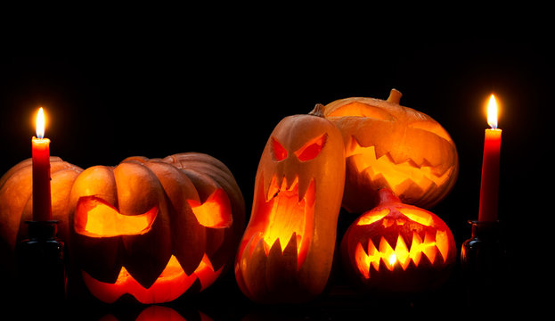 Photo of halloween pumpkins with burning mouths, candles on empty black background