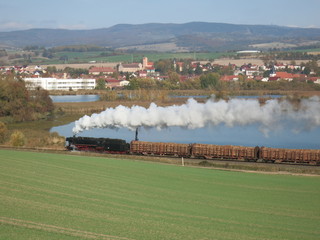 ein See, davor ein mit Dampflok bespannter Holzzug