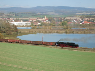ein See, davor ein mit Dampflok bespannter Holzzug