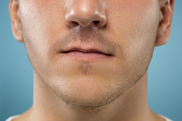 Obraz premium Caucasian young man's close up portrait on blue studio background. Beautiful male model with well-kept skin. Concept of human emotions, facial expression, sales, ad, beauty. Lips and cheeks.