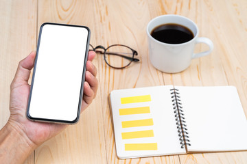 Hand holding blank screen smart phone with office table background