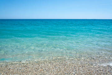 Obraz premium Turquoise sea, slightly rocky beach, mountains in the distance