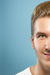 Fototapeta premium Caucasian young man's close up portrait on blue studio background. Beautiful male model with well-kept skin. Concept of human emotions, facial expression, sales, ad, beauty. Smiling, laughting.