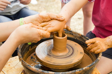 A close up view on ceramic production process on potter's wheel with children. Clay crafts with kids concept.