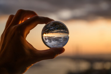 Fototapeta na wymiar The hand holds glass ball which reflects sunset sky over city.