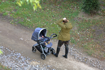 Obraz premium Woman with a baby stroller walks through the the picturesque autumn park