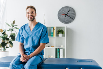 cheerful doctor looking at camera while sitting in clinic