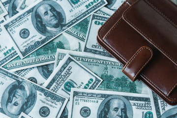 top view of brown leather wallet on dollar banknotes